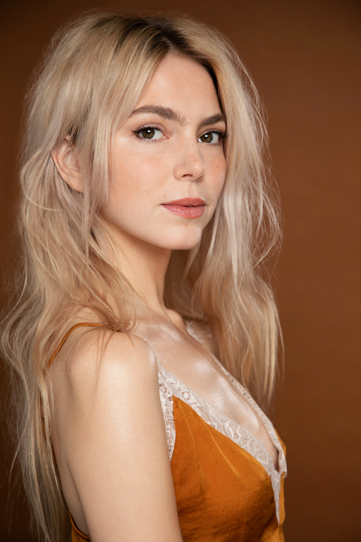 Alyson Gorske in a studio portrait, wearing a burnt orange satin top with lace trim and looking over her shoulder toward the camera.